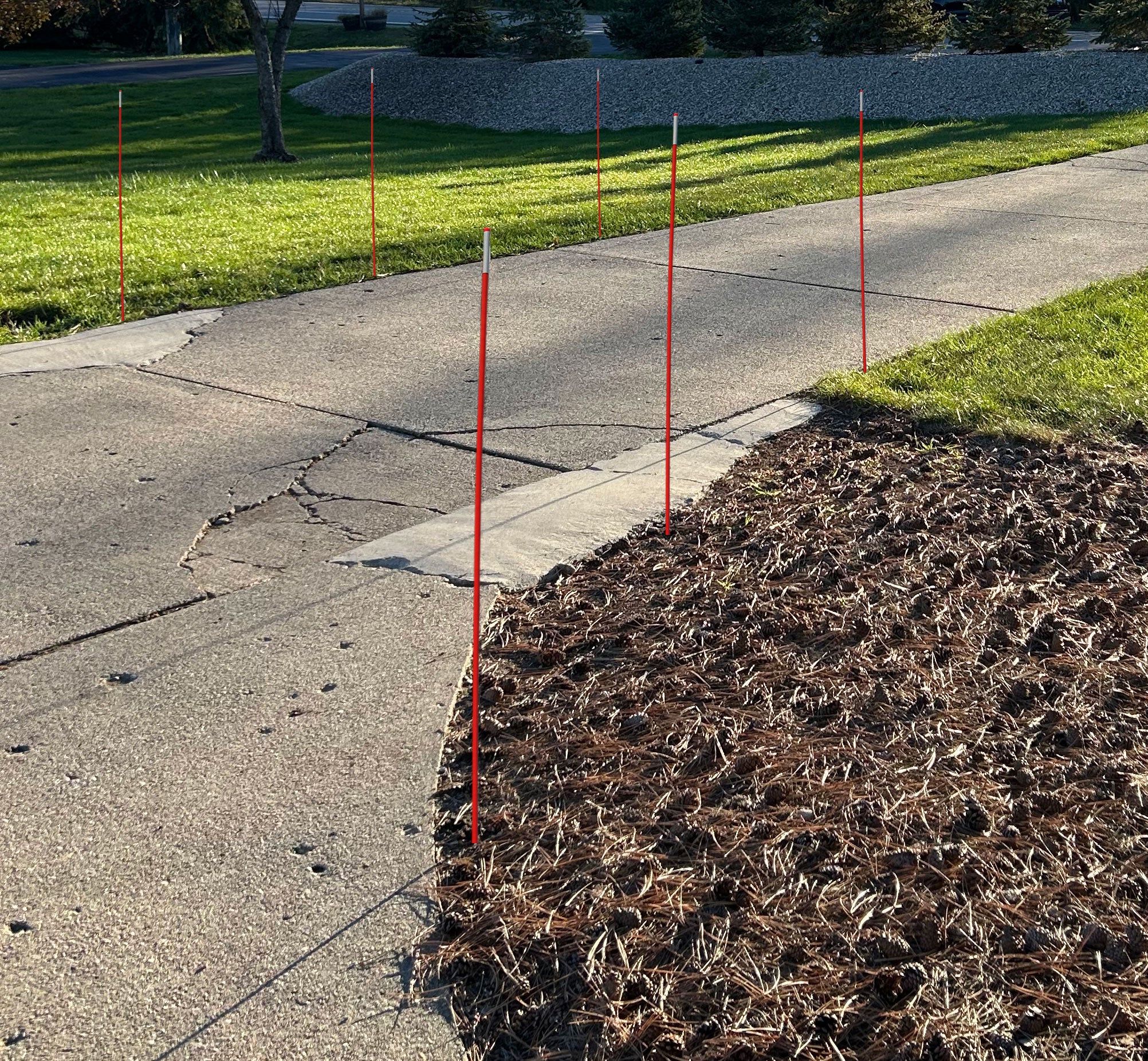 Red stakes marking a boundary on a sidewalk next to a grassy area