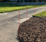 Red stakes marking a boundary on a sidewalk next to a grassy area