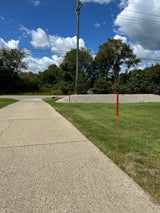 Sidewalk next to a grassy area with trees under a blue sky.